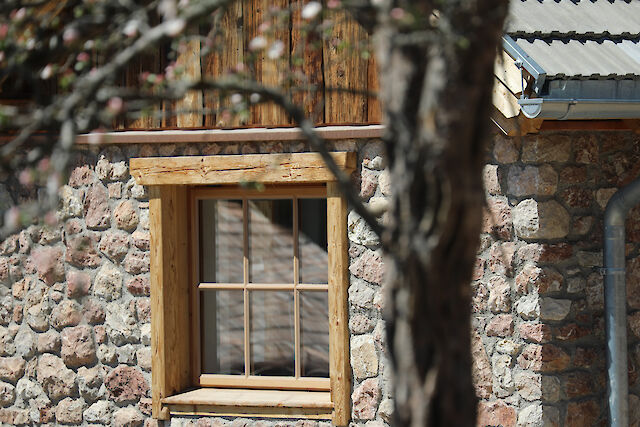 Schmiedgut - Natursteinfassade der alten Schmiede mit Sprossenfenster vor Obstbaum